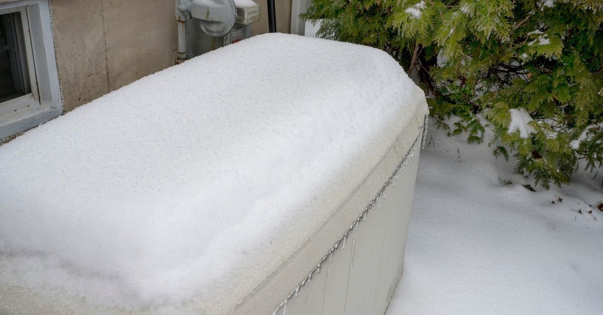 A close-up of a standby generator installed just outside a home next to a bush covered in ice and sn