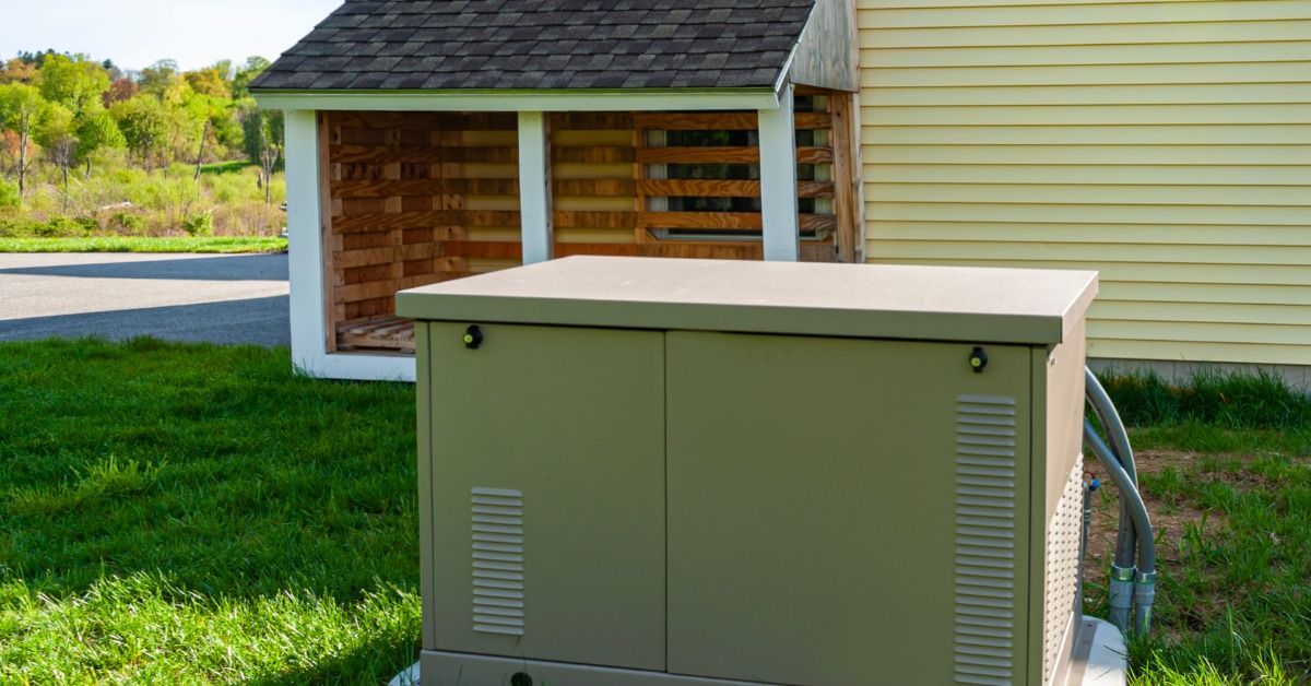 A residential standby generator on a concrete platform on grass outside a yellow home.