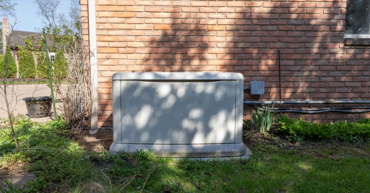 A residential standby generator on a cement slab outside a home with a brick exterior on a sunny day
