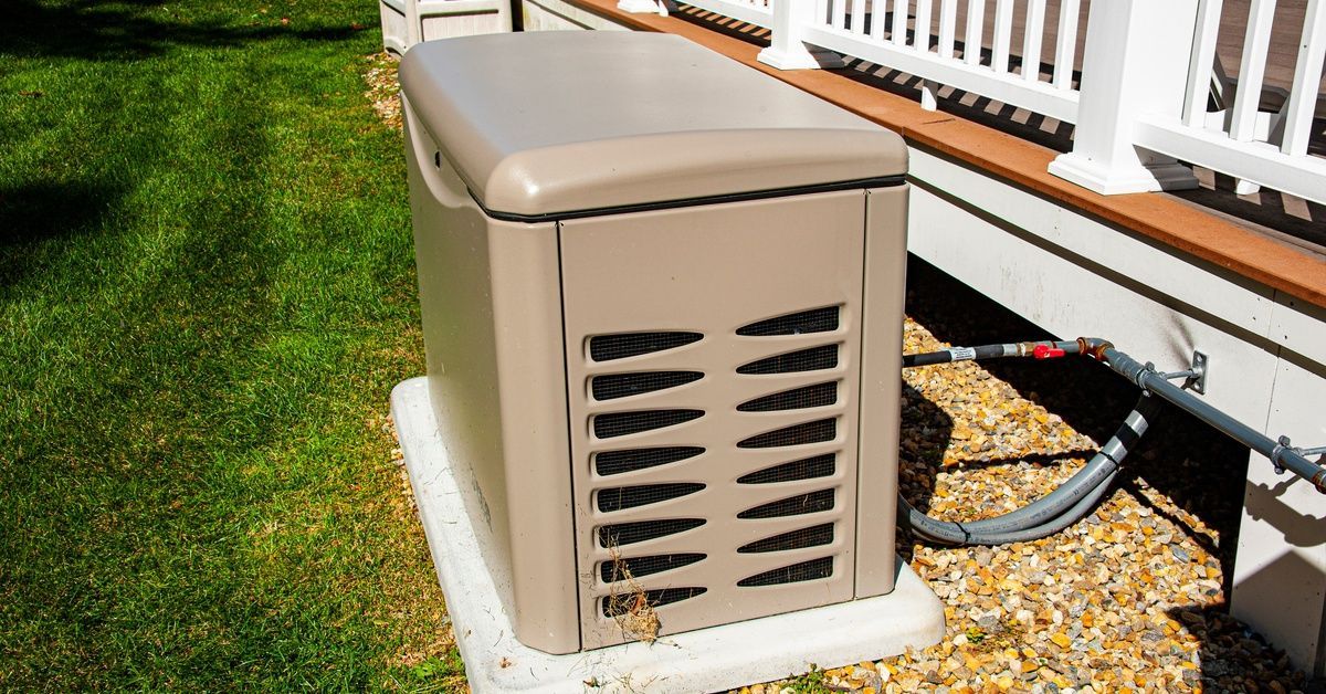 A standby home generator sits on a concrete pad beside a house, connected to a fuel line.