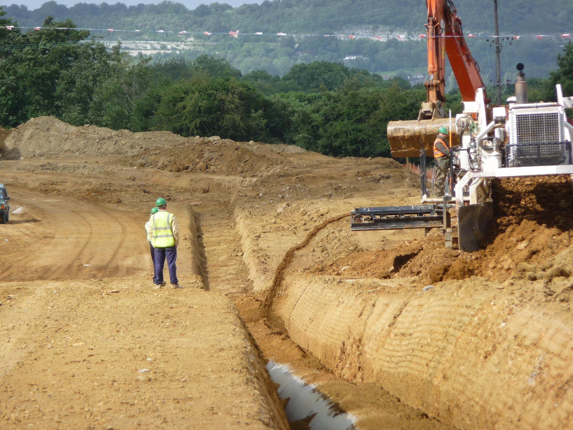 Construction site with excavator digging a trench beside a worker in a safety vest
