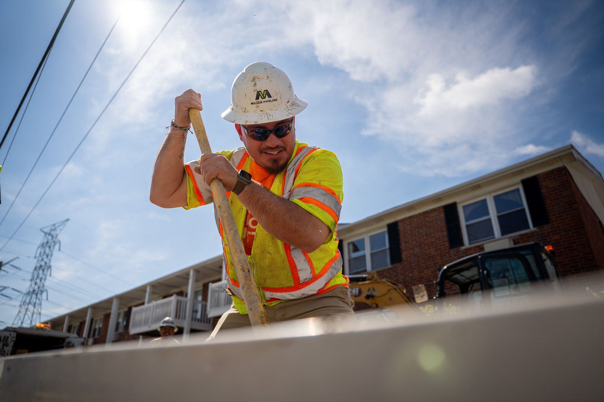 Construction worker in hard hat and safety vest using a tool at a building site under a blue sky