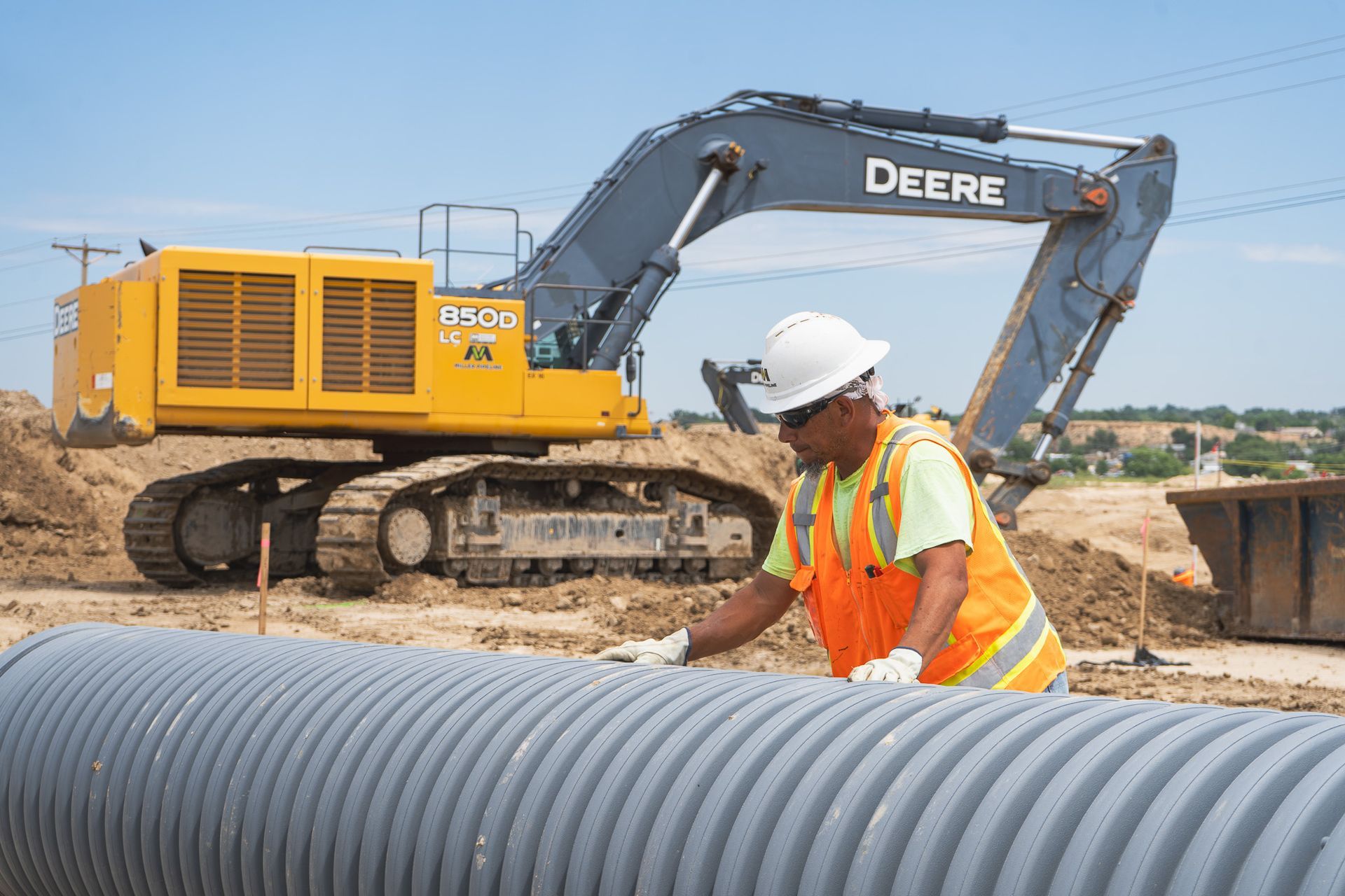 Construction worker inspecting corrugated pipe beside a yellow excavator at a site