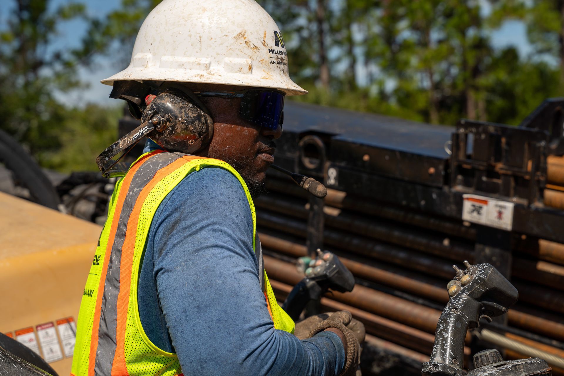 Worker in white hard hat and reflective vest handling equipment at an industrial site