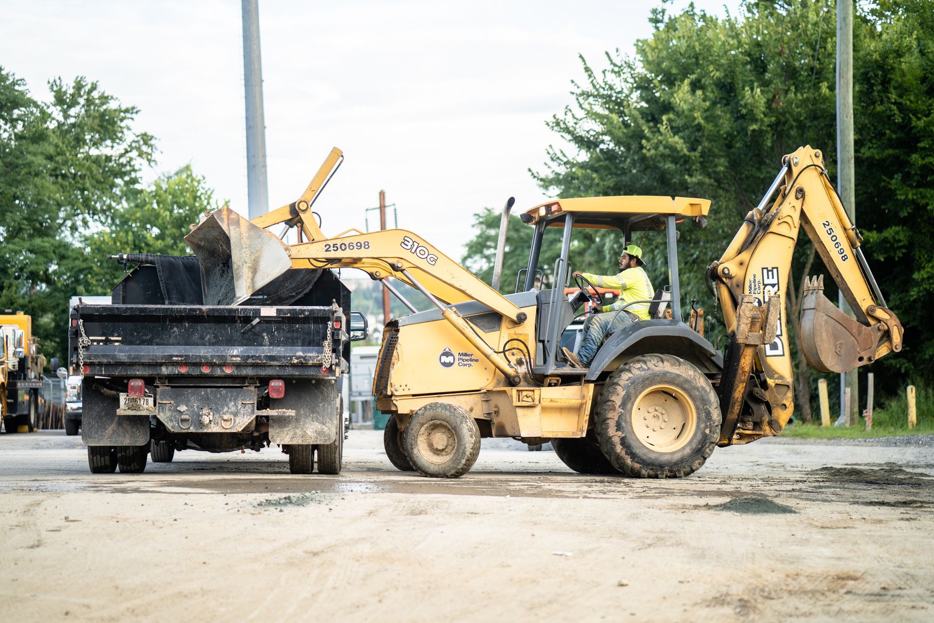 Yellow backhoe loader dumping dirt into a black dump truck on a construction site