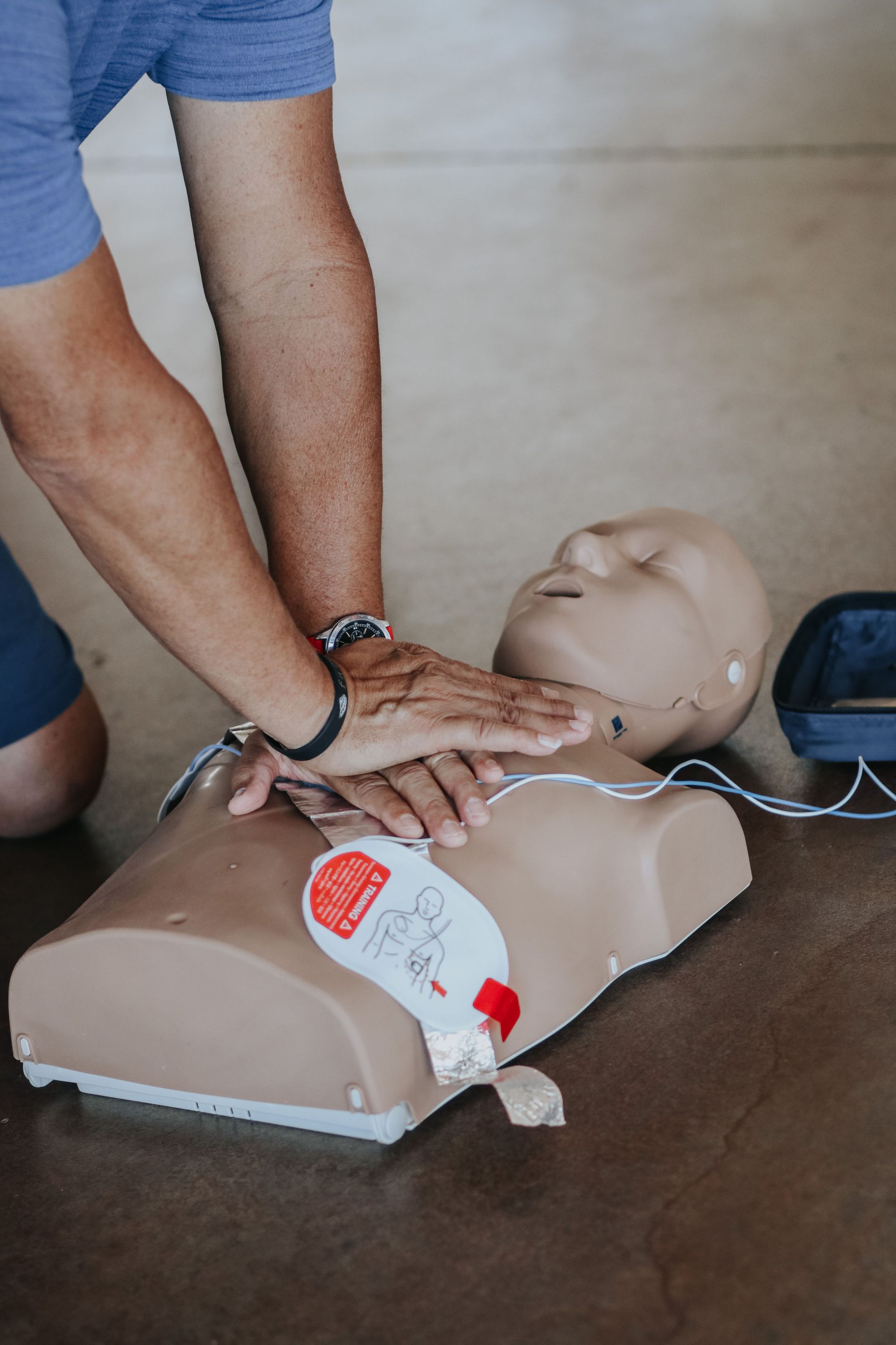 Person performing CPR on a training manikin with visible electrode pads on a table