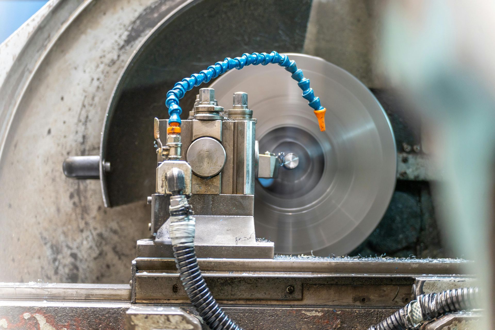 Metal lathe cutting a large silver disk with a blue coolant hose in an industrial workshop