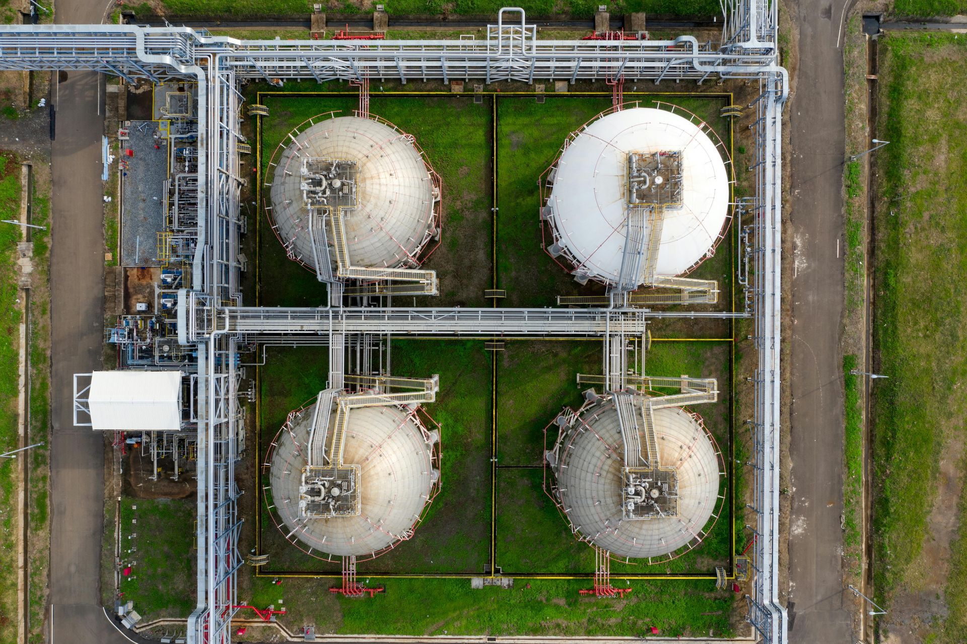 Aerial view of four white storage tanks in an industrial facility with pipelines and green ground.