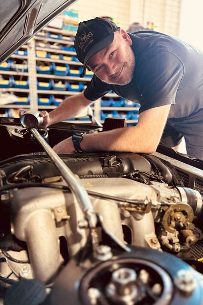 Mechanic smiling while working on a car engine in a garage