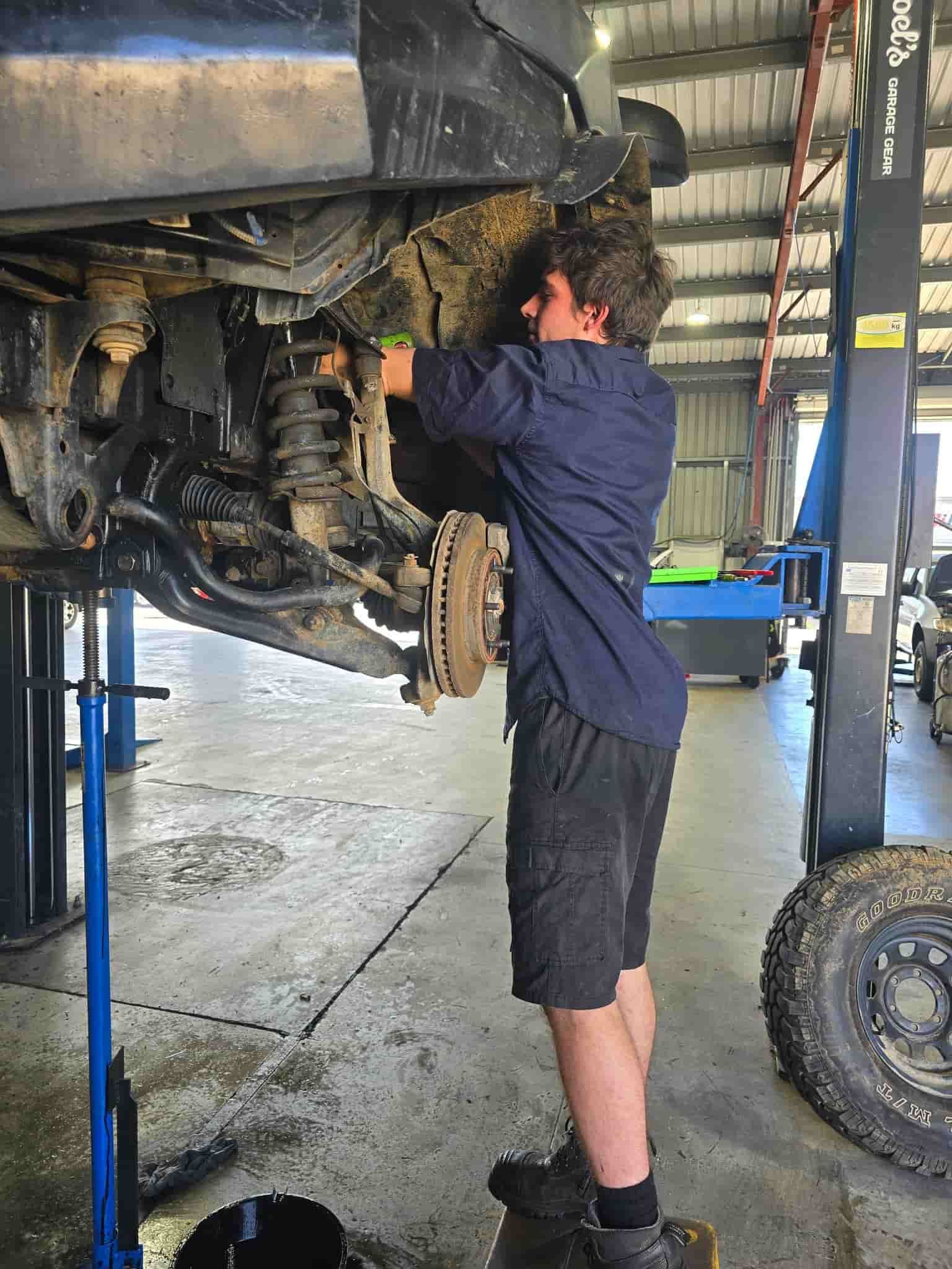 A Man Is Working On The Underside Of A Vehicle In A Garage — M8S Rates Mechanical In Gladstone Central, QLD