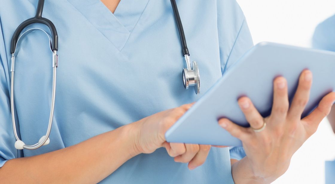 A nurse with a stethoscope around her neck is using a tablet