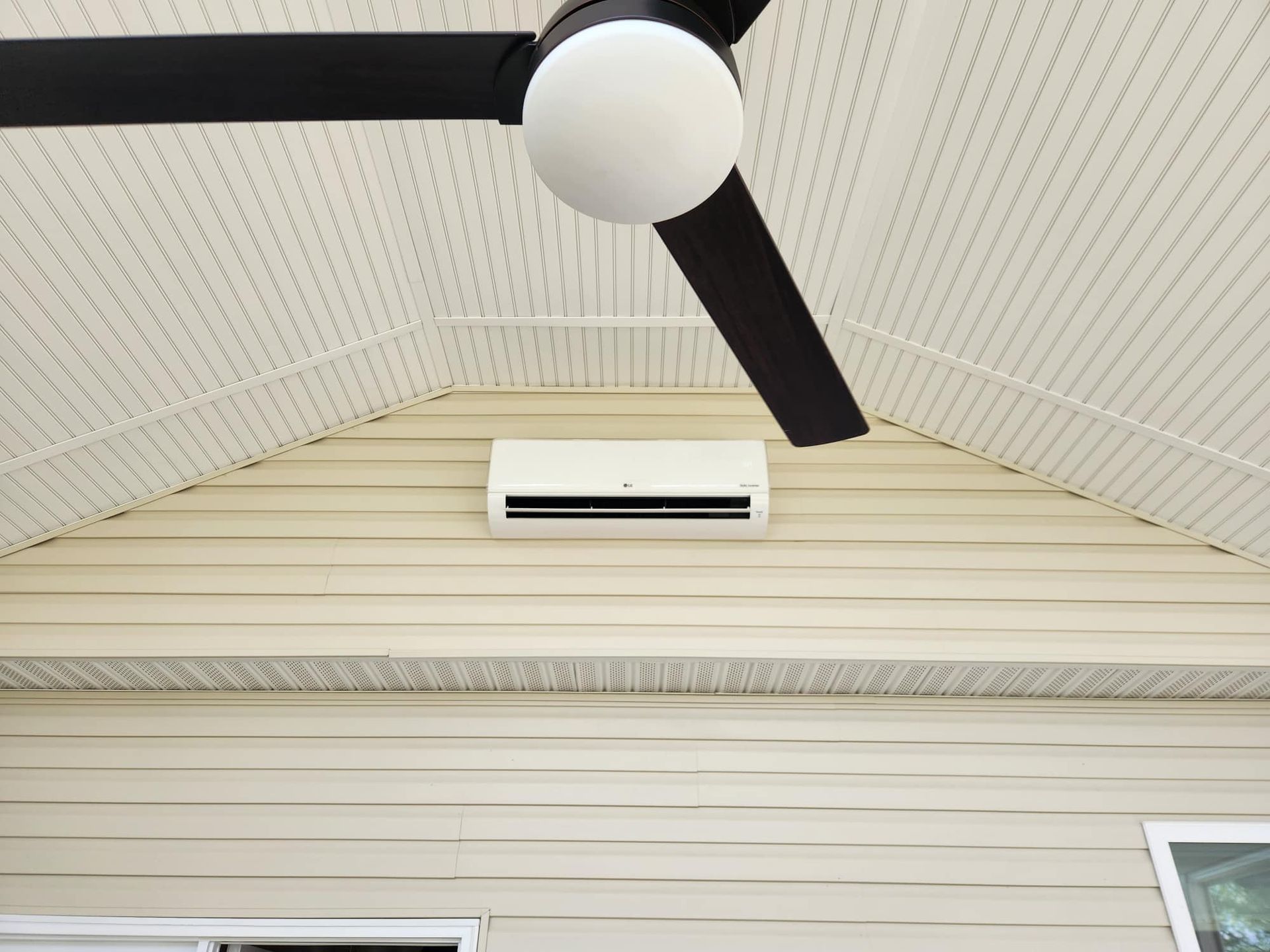 Ceiling fan and wall-mounted air conditioner on a white paneled porch ceiling