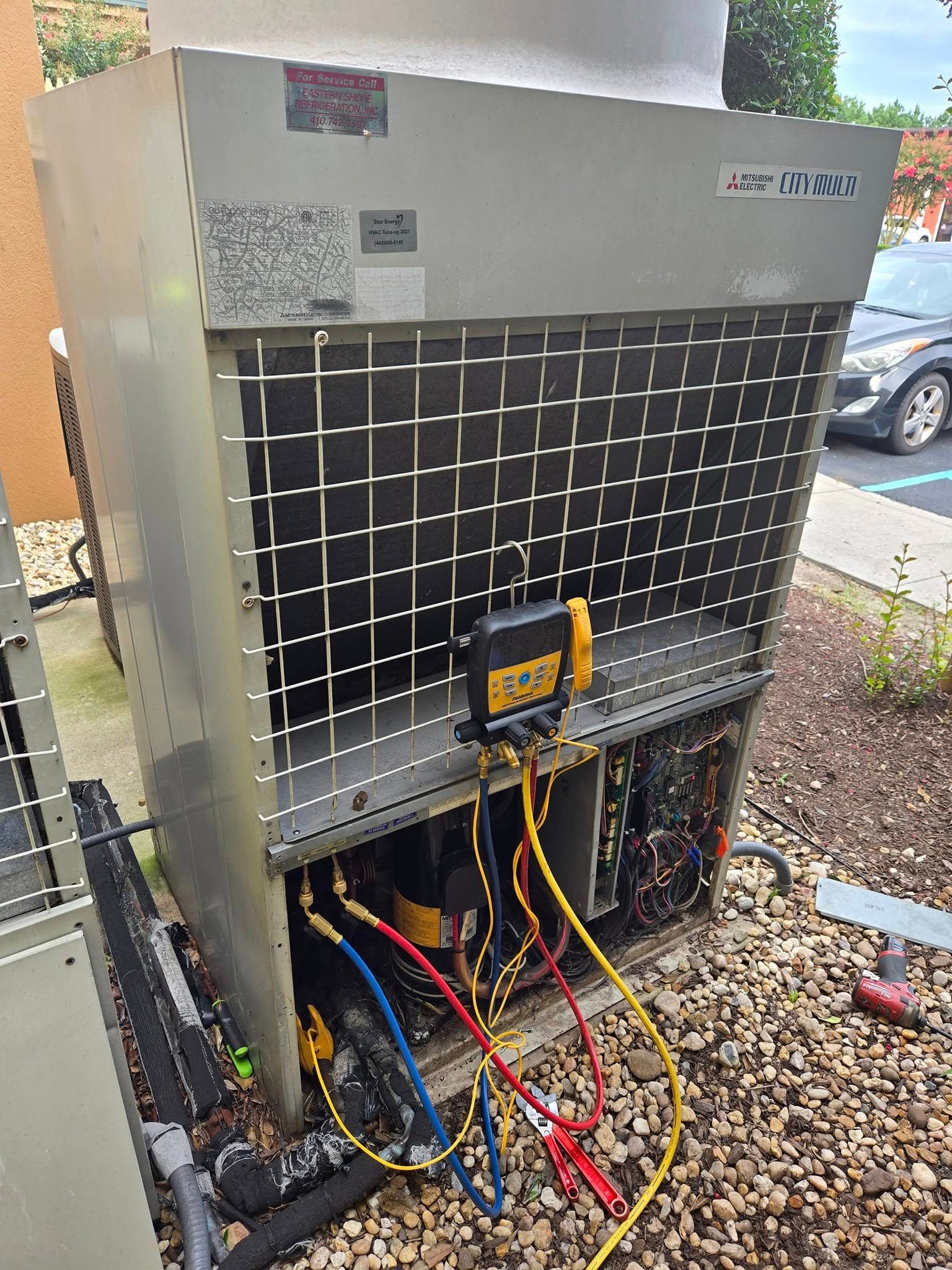 Outdoor industrial HVAC unit with front grille, exposed wires, and maintenance tools on the ground
