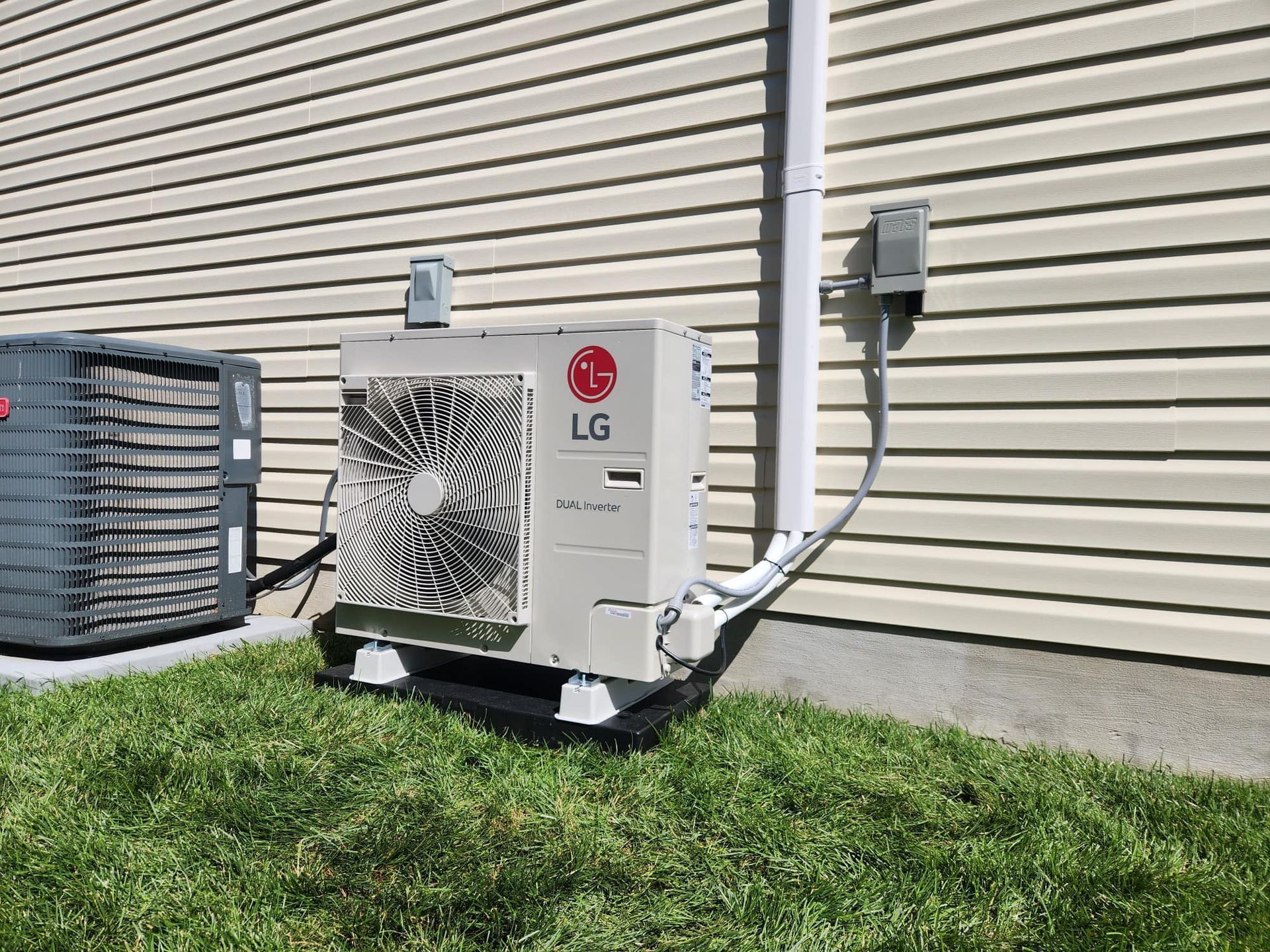 Outdoor LG air conditioning unit beside a beige building wall and grass lawn.