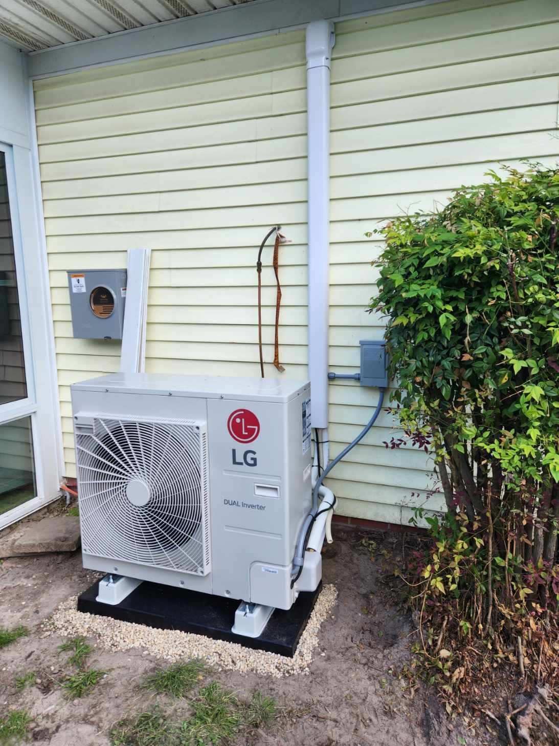 LG outdoor HVAC unit beside a house wall, with pipes and a shrub nearby