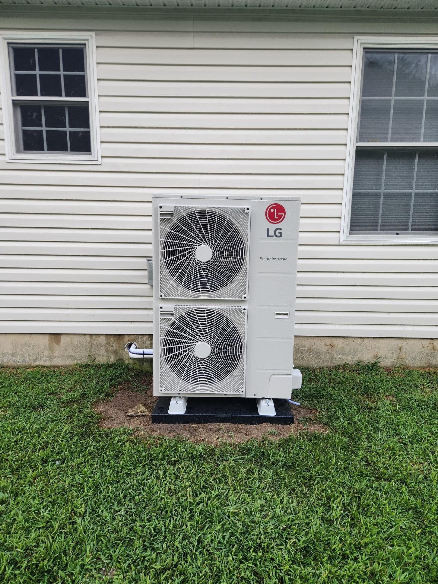 LG outdoor air conditioner unit on a black pad beside a white house wall.