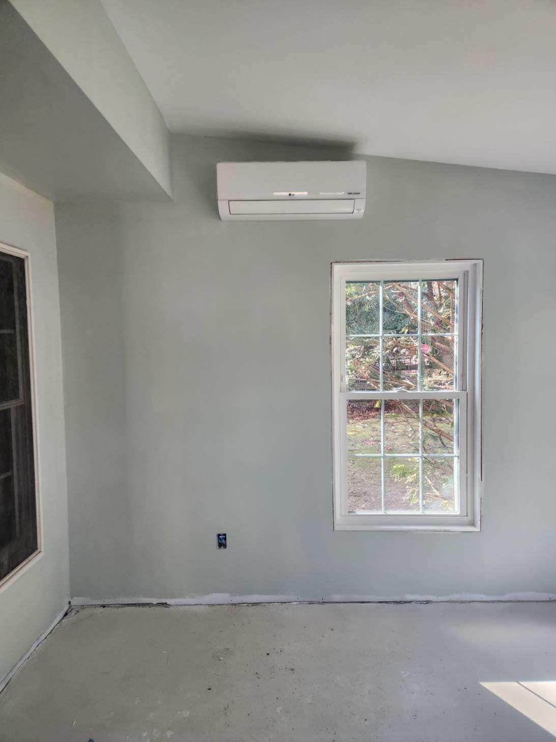 Empty gray room with wall-mounted air conditioner and a window letting in daylight