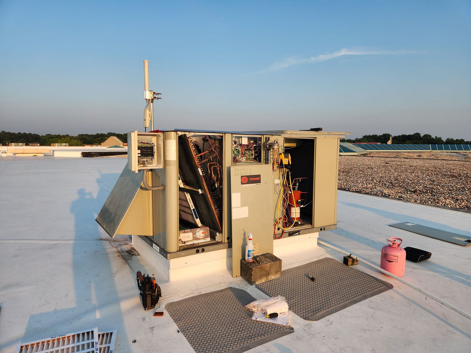 Open industrial equipment on a rooftop under clear sky, with tools and mats nearby