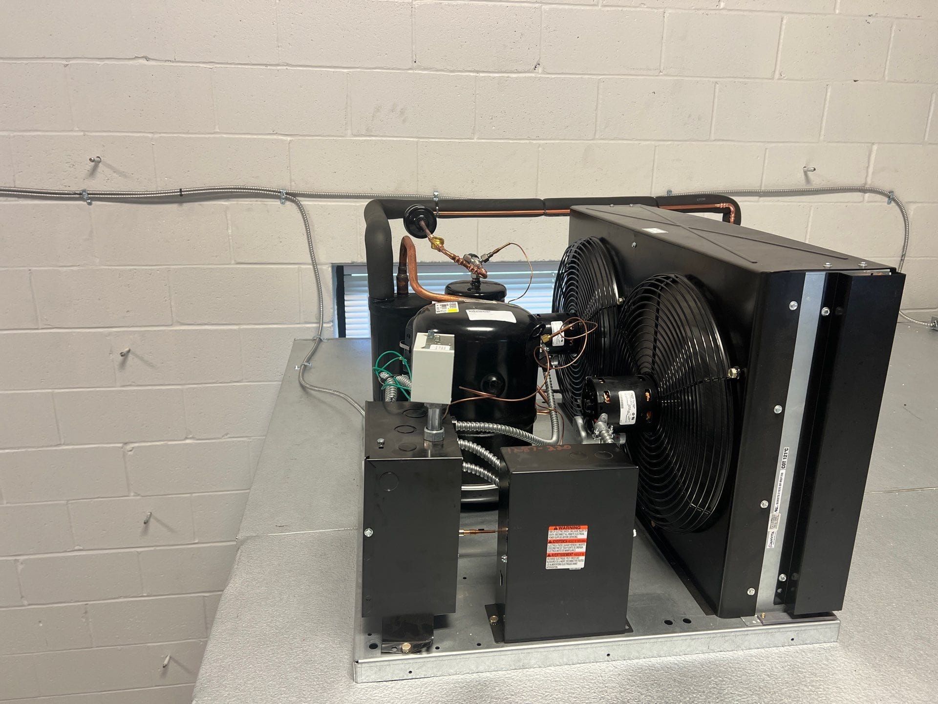Industrial machine with a large black fan and metal components against a cinderblock wall