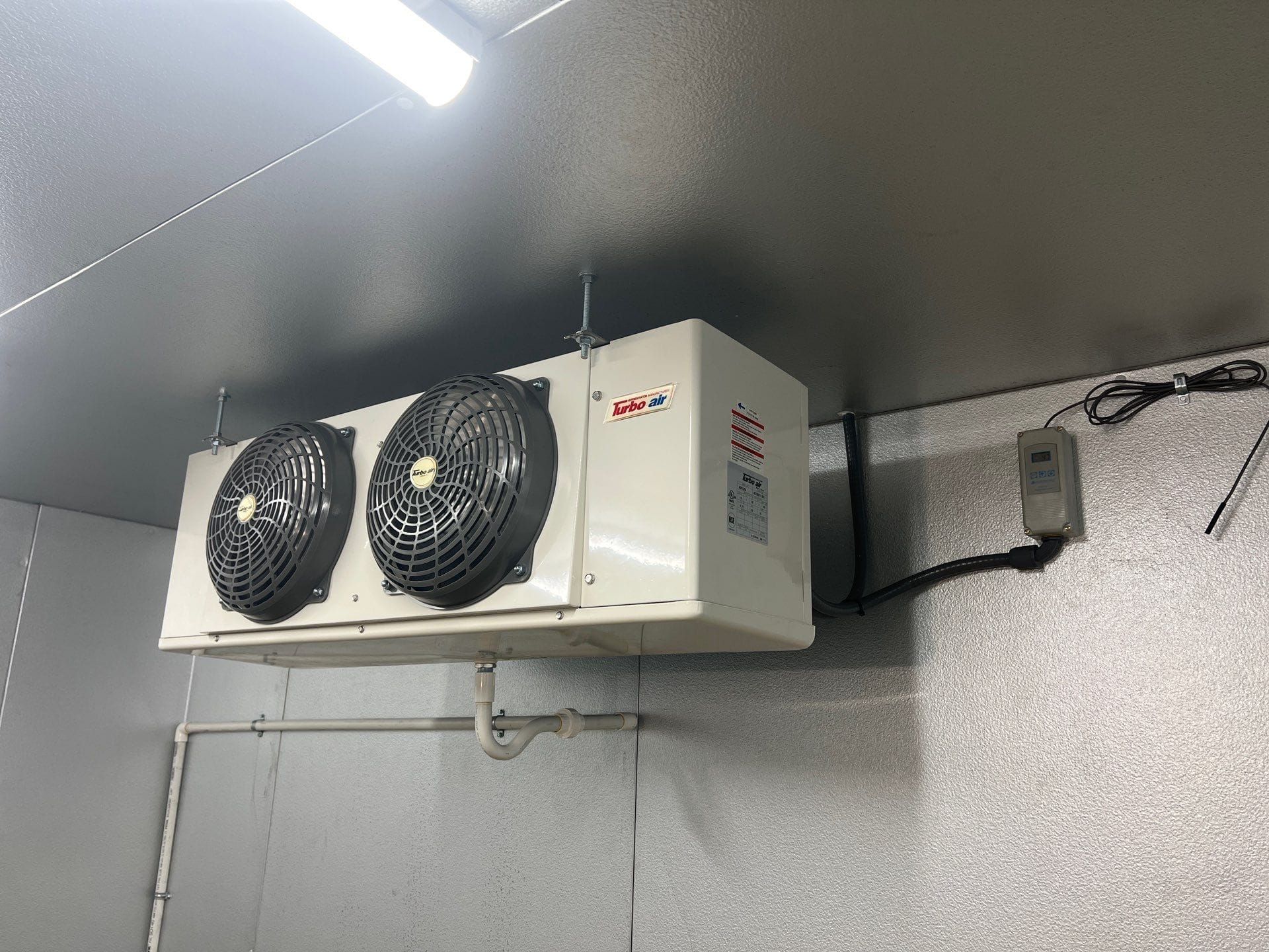 Ceiling-mounted refrigeration unit with two black fans in a gray industrial room