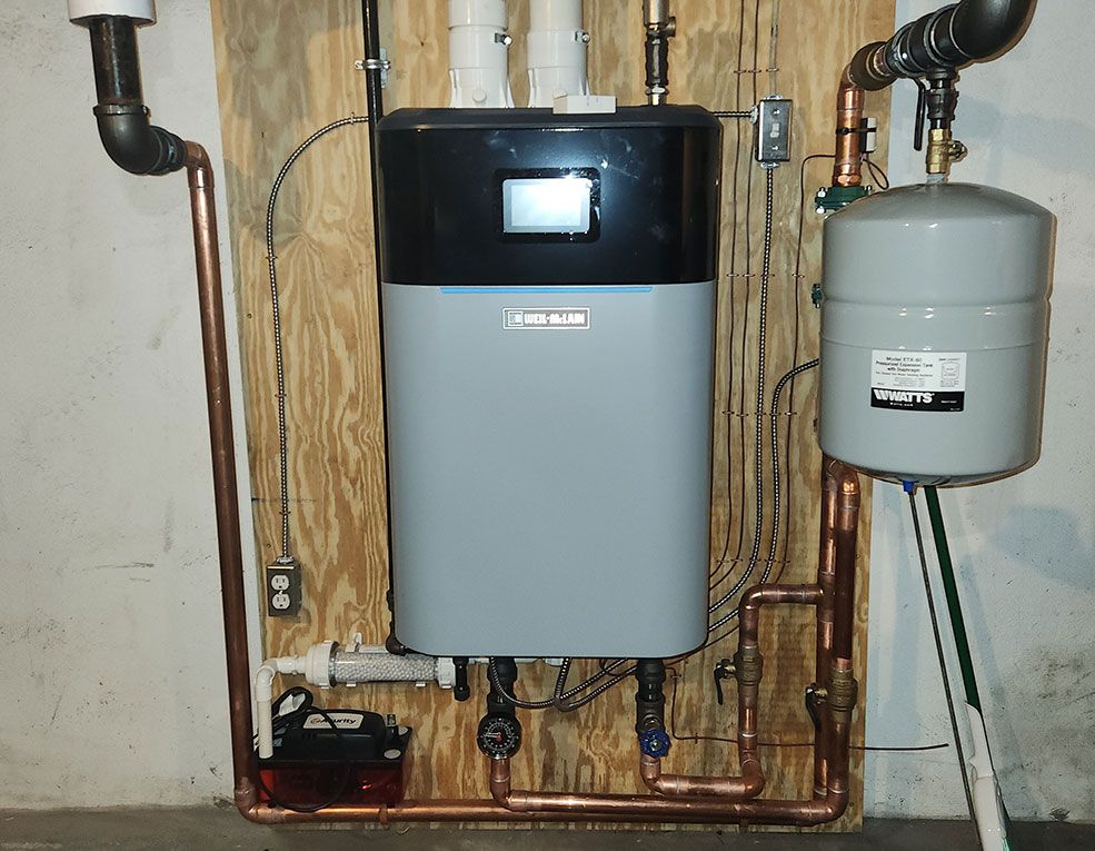 Wall-mounted boiler and gray expansion tank in a utility room, with exposed pipes and copper tubing.