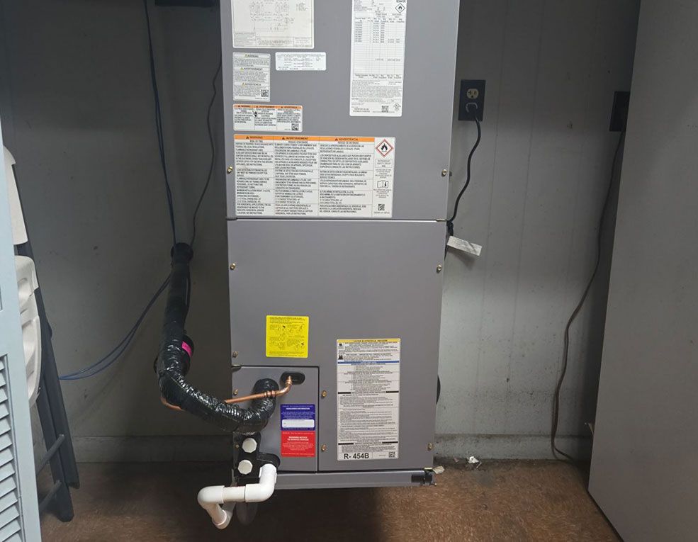 Gray HVAC unit with labels, connected black hose, and white drain pipe in an indoor utility room