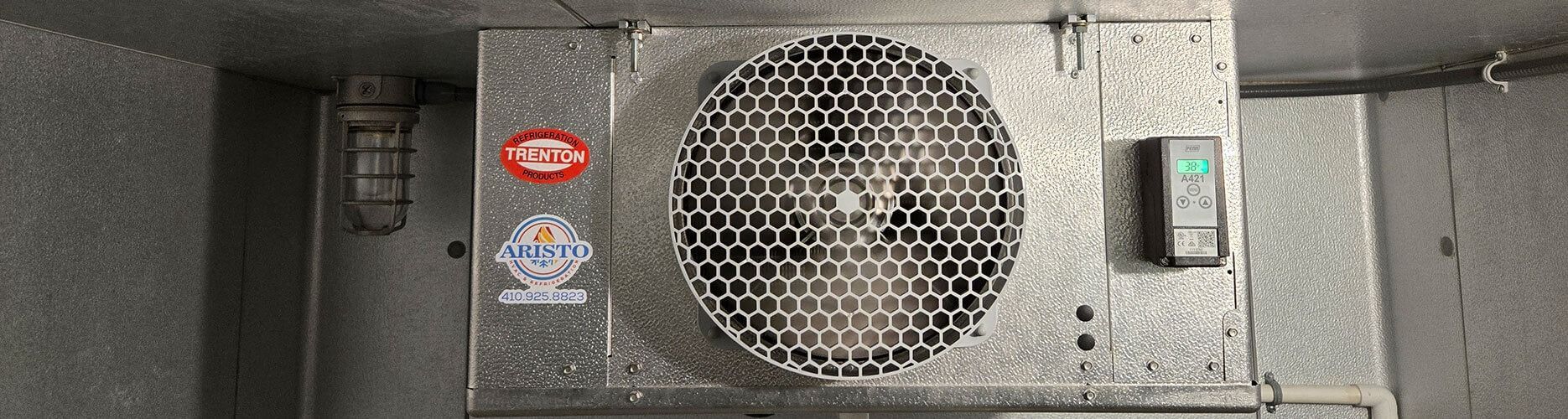 Industrial metal machine with a large fan grille, warning stickers, and a switch panel on a gray surface