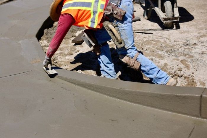 Construction worker smoothing wet concrete curb with a trowel, outdoors.