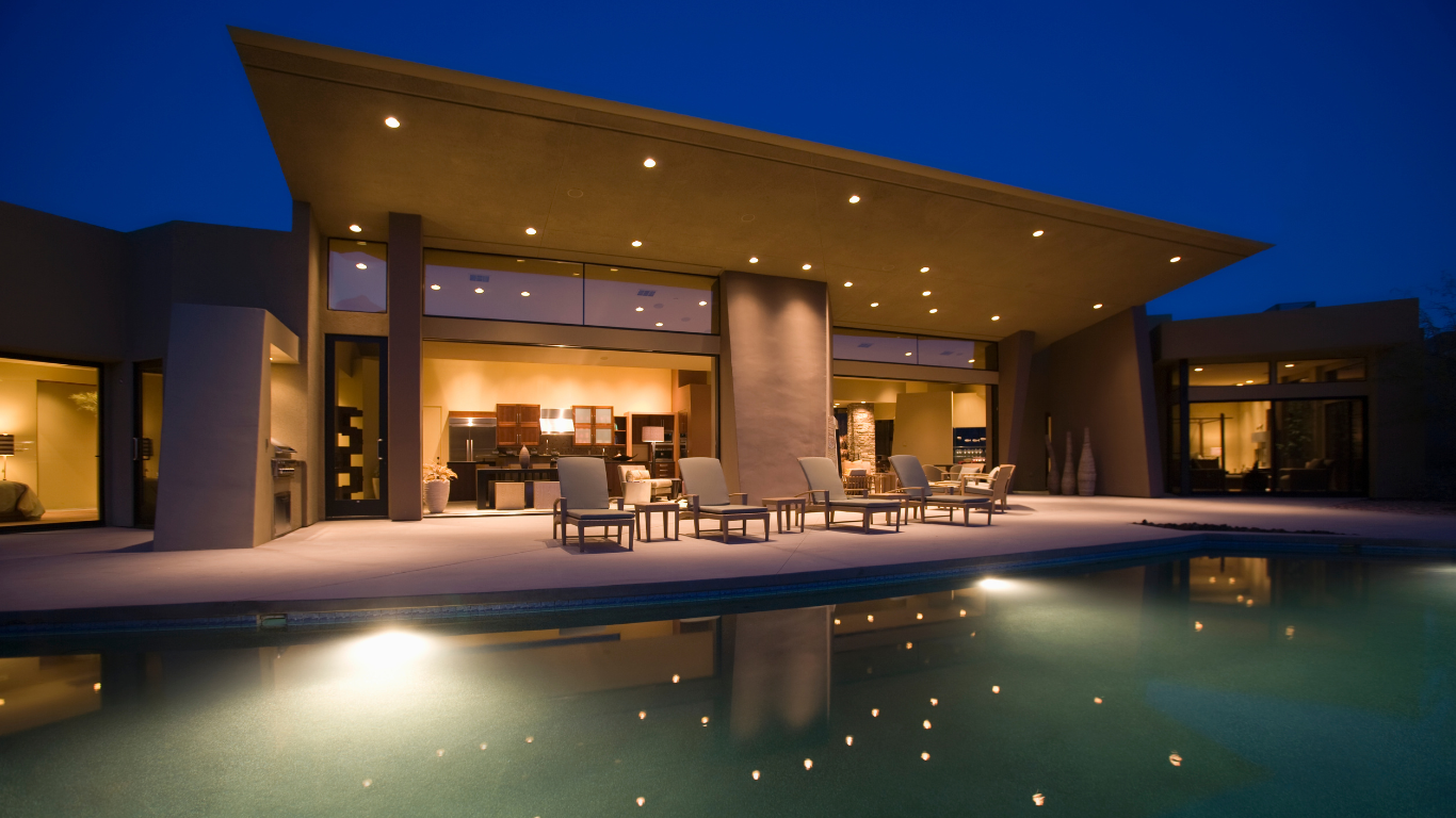 Modern villa patio at dusk with lit seating area and a swimming pool reflecting the lights