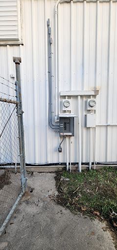 A white building with a chain link fence and electrical outlets on the side. A white building with a chain link fence and electrical outlets on the side.