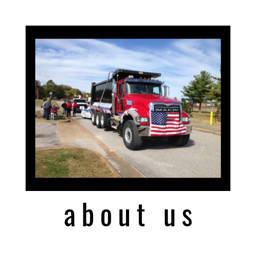 Red truck with American flag grille driving at an event, with “about us” text below