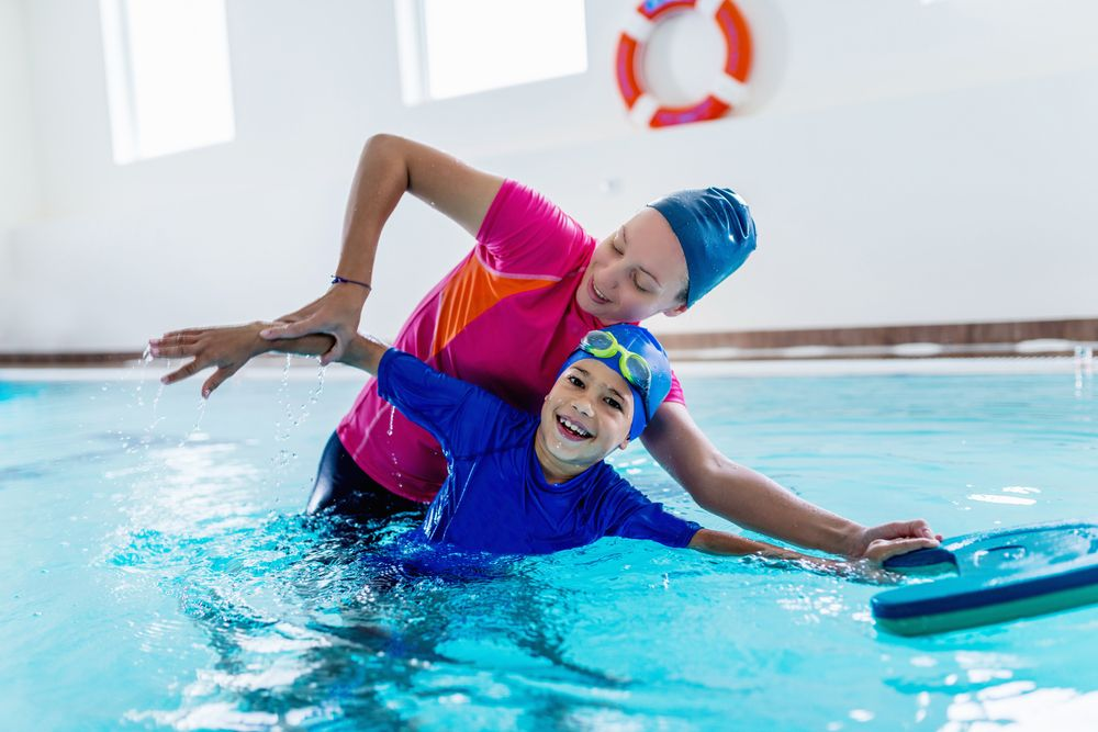 Two swimmers in colorful caps practicing a pool rescue in an indoor swimming pool