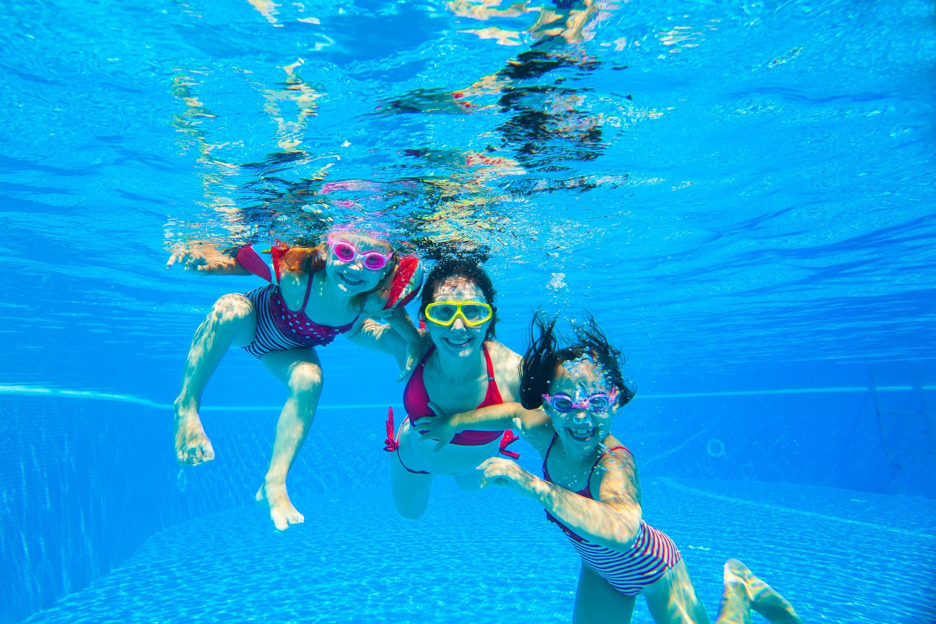 Three snorkelers swimming underwater in a bright blue pool