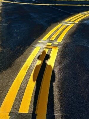 Shadows of two people cast on a winding yellow center line on a dark road