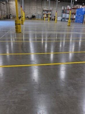 Empty warehouse floor with yellow safety lines and industrial shelving in the background