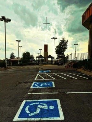 Accessible parking spaces in a lot near a building and cross-shaped monument under a cloudy sky