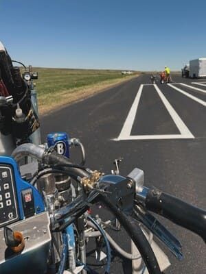 Motorcycle view on highway shoulder near roadwork, with trucks ahead and clear sky.