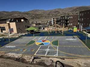Colorful playground court with painted game circles, surrounded by apartment buildings and mountains.