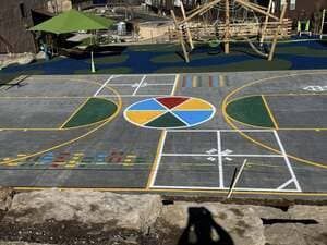 Colorful outdoor court with geometric painted shapes and a multicolored circle in the center, near wooden structures