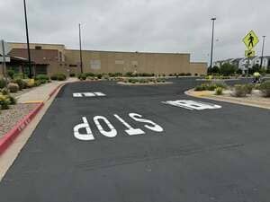 Parking lot lane with large white STOP marking and a pedestrian crossing sign near a beige building