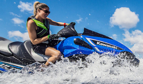 Donna che cavalca un jet ski Kawasaki blu e nero sull'acqua, creando uno schizzo.