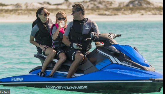 Una famiglia su una Yamaha WaveRunner blu in acque limpide; indossano giubbotti di salvataggio e occhiali da sole.