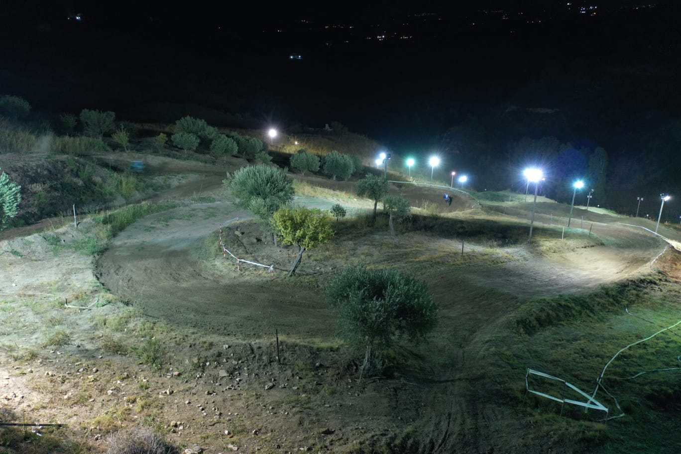 Pista per moto da cross illuminata di notte con luci intense, situata su una collina.