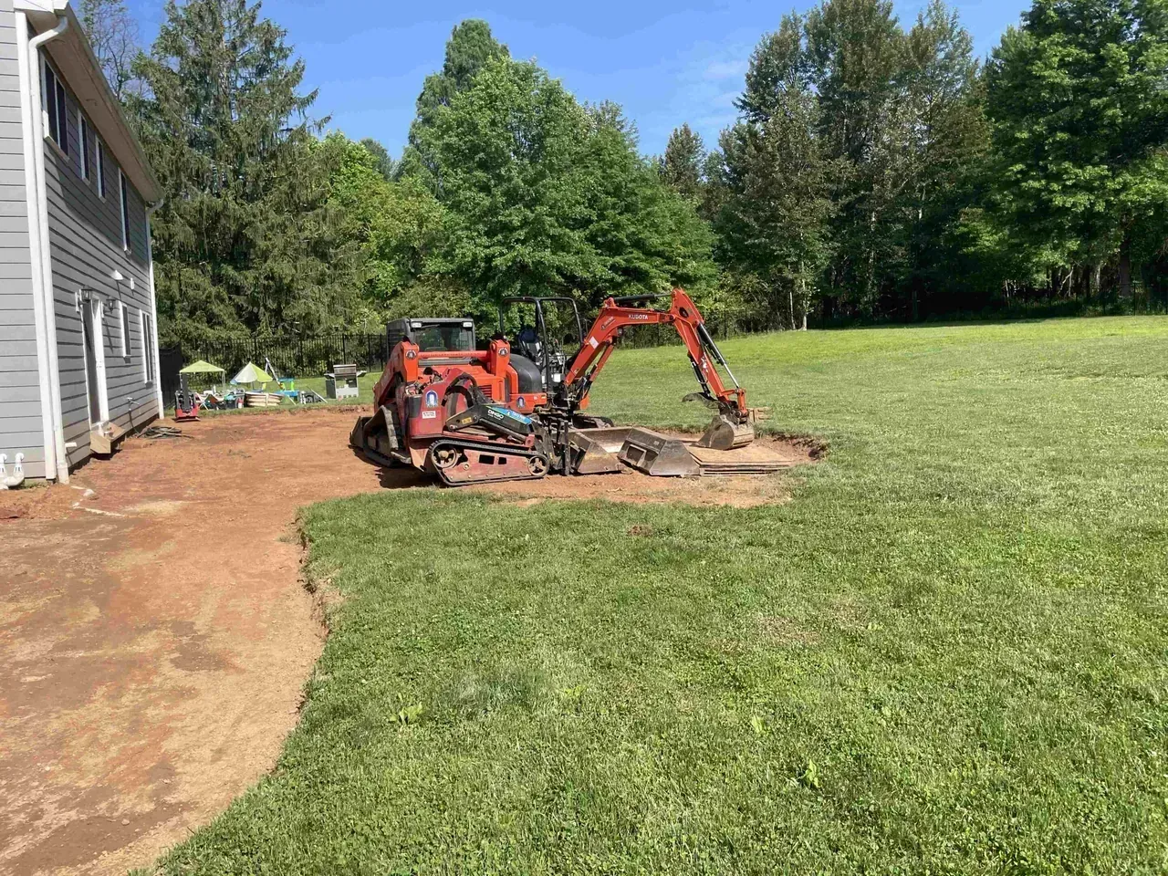 Compact excavator and equipment parked on lawn after residential land grading and yard regrade work.