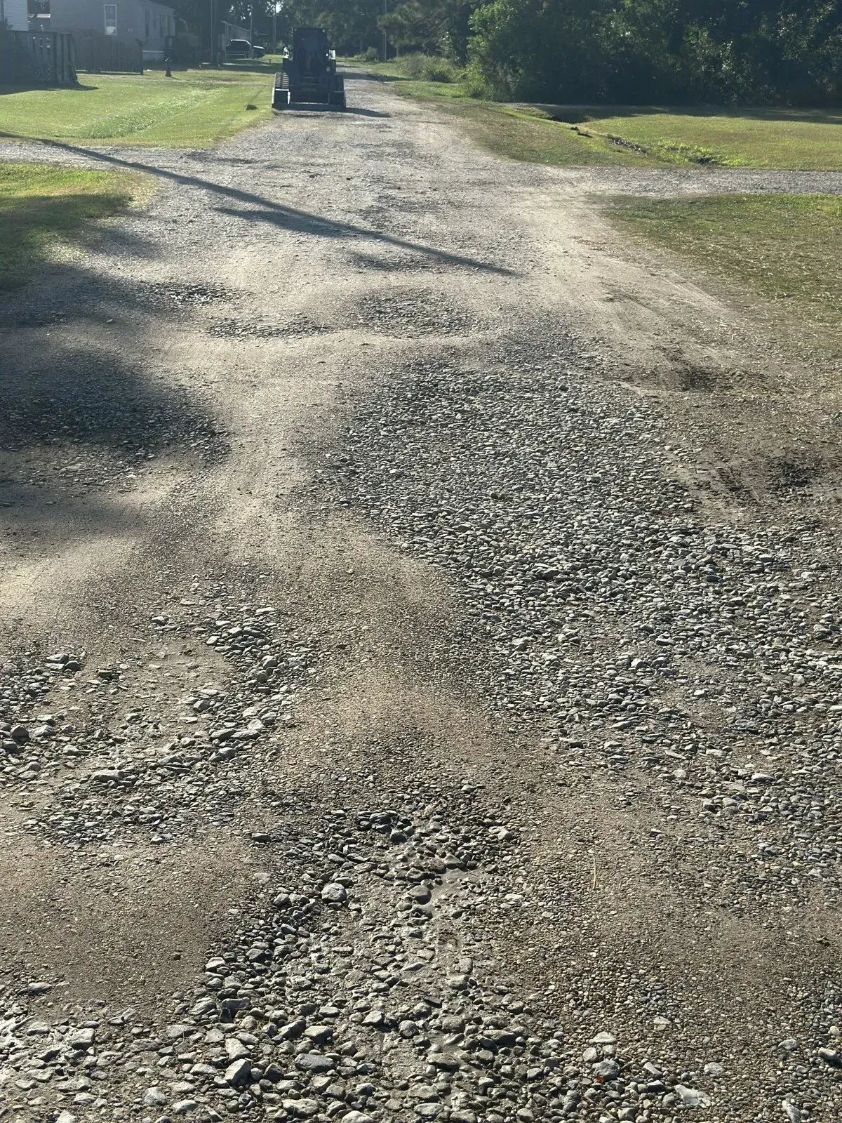 Uneven gravel driveway surface with rutting prior to regrading and repair.
