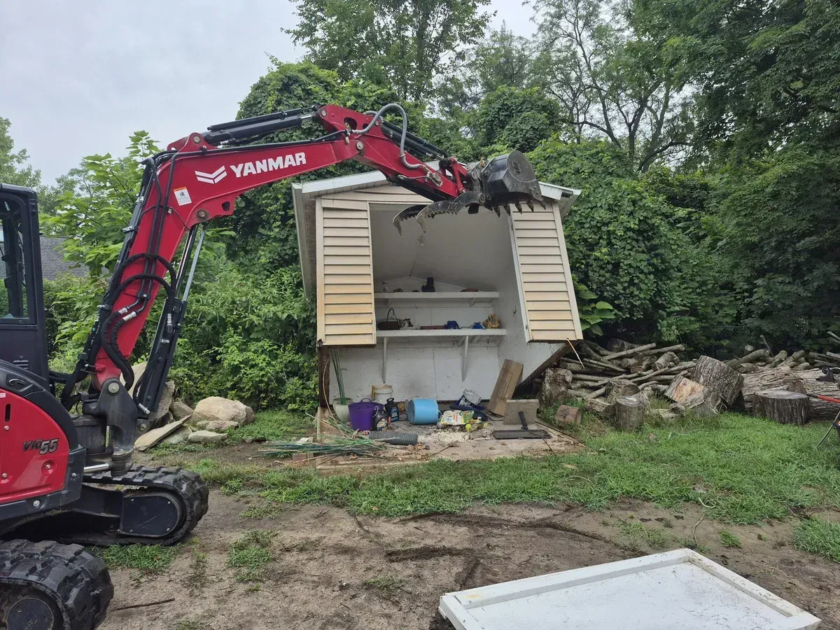 Mini excavator tearing down a wooden shed during residential demolition