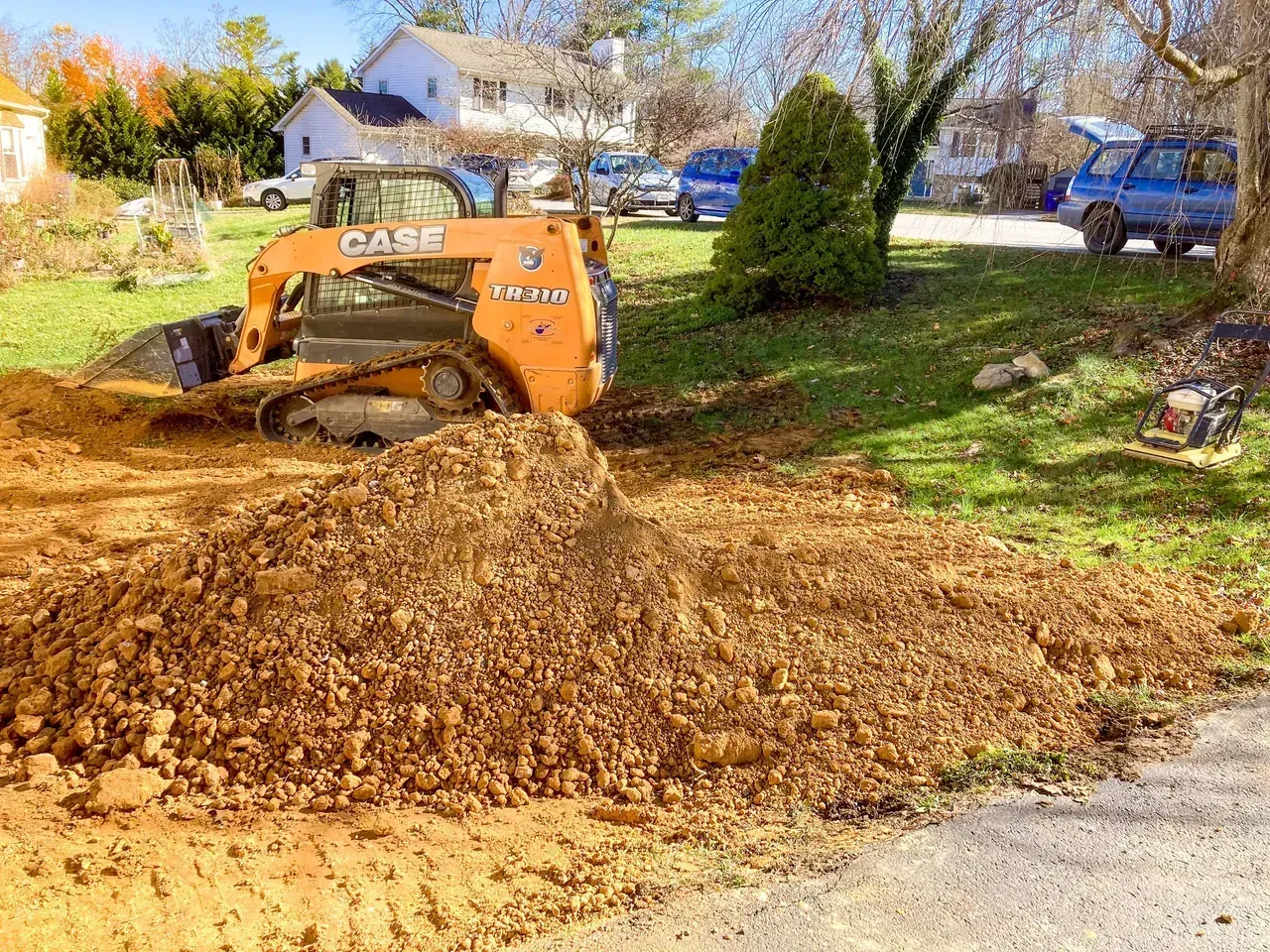 Track loader leveling dirt and spreading fill material in a residential yard.