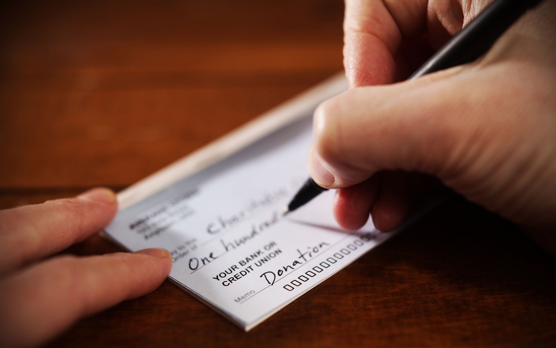 Una persona está escribiendo un cheque por cien dólares.