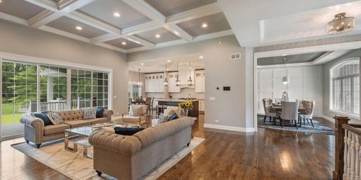 Bright open-concept living room and dining area with gray sofas, coffered ceiling, and large windows