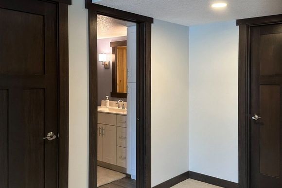 Empty hallway with dark wood doors and an open bathroom doorway showing a sink and mirror.